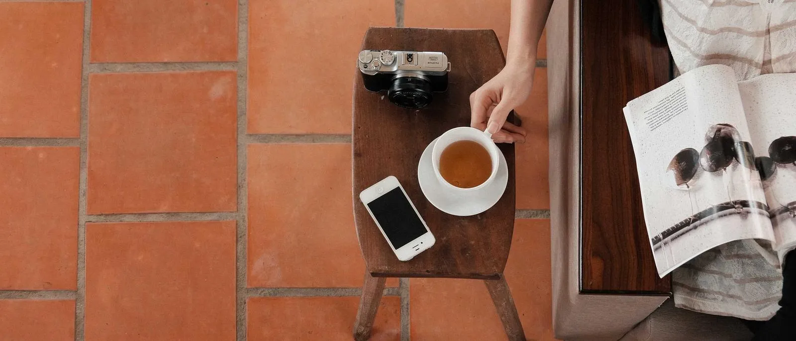 Hand mit Kaffeetasse, Smartphone und Zeitschrift auf einem Tisch